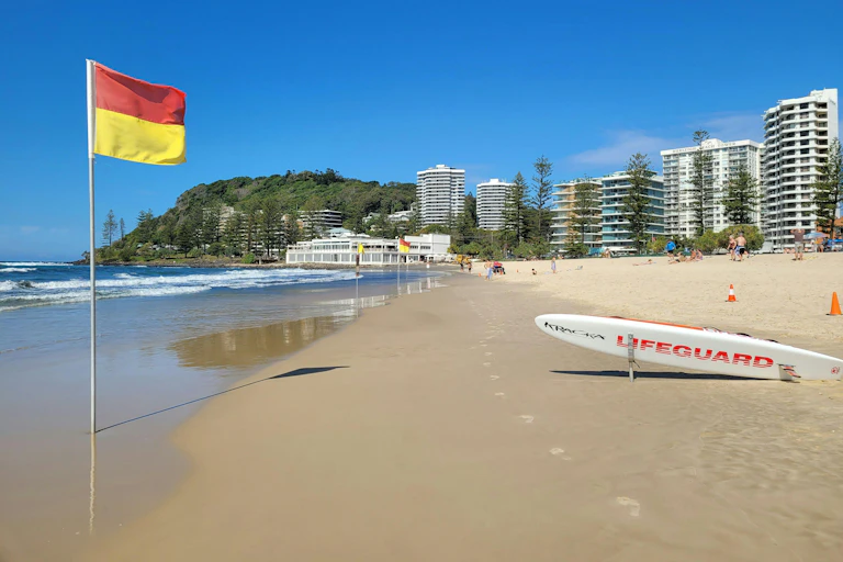 A red and yellow flag and a surfboard reading 'LIFEGUARD' on an empty beach.