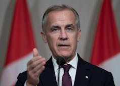 Un hombre con cabello corto gris oscuro hace gestos mientras habla.