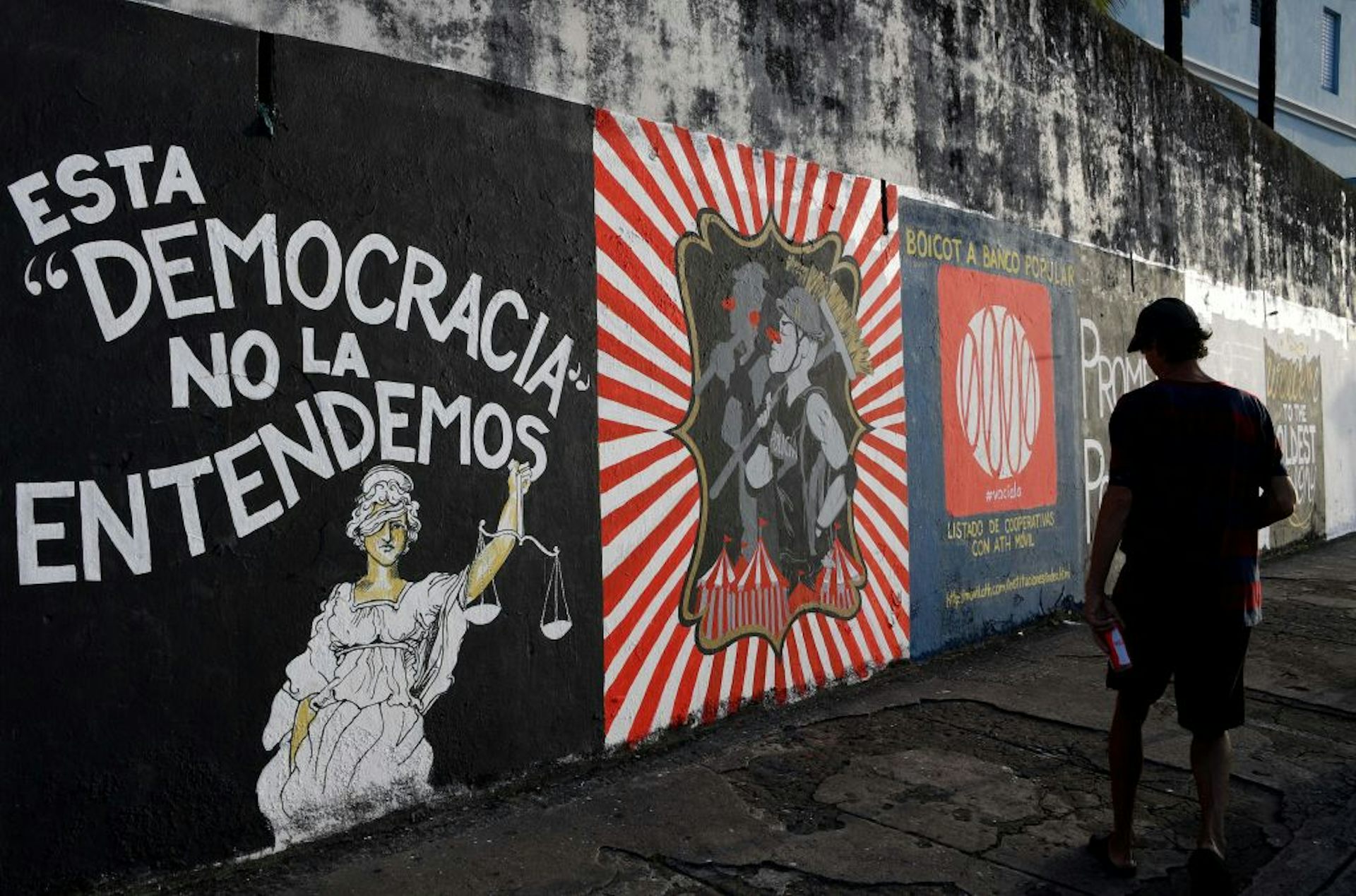 A man walks past a wall with several different political murals painted on it.