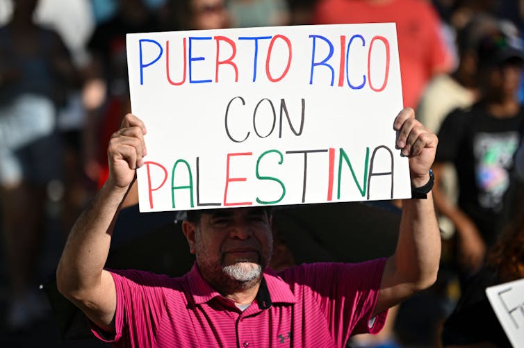 Dangerous Bunny and Puerto Rican Muslims: How each remix what it approach to be Boricua 3 A man in a red shirt, standing amid a crowd, holds a sign that says, in Spanish, 'Puerto Rico with Palestine.'