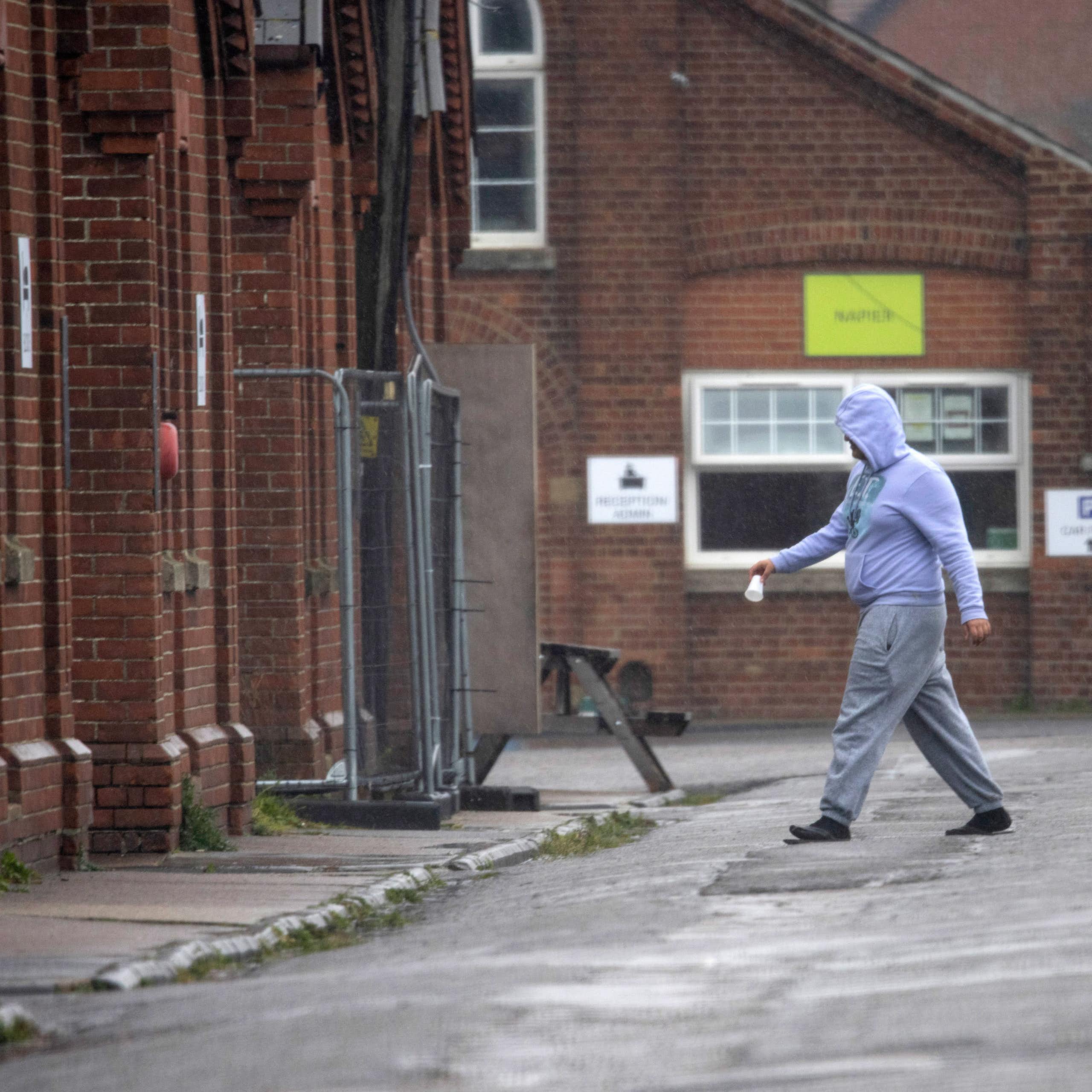 A man in hoodie and joggers walks in Napier Barracks