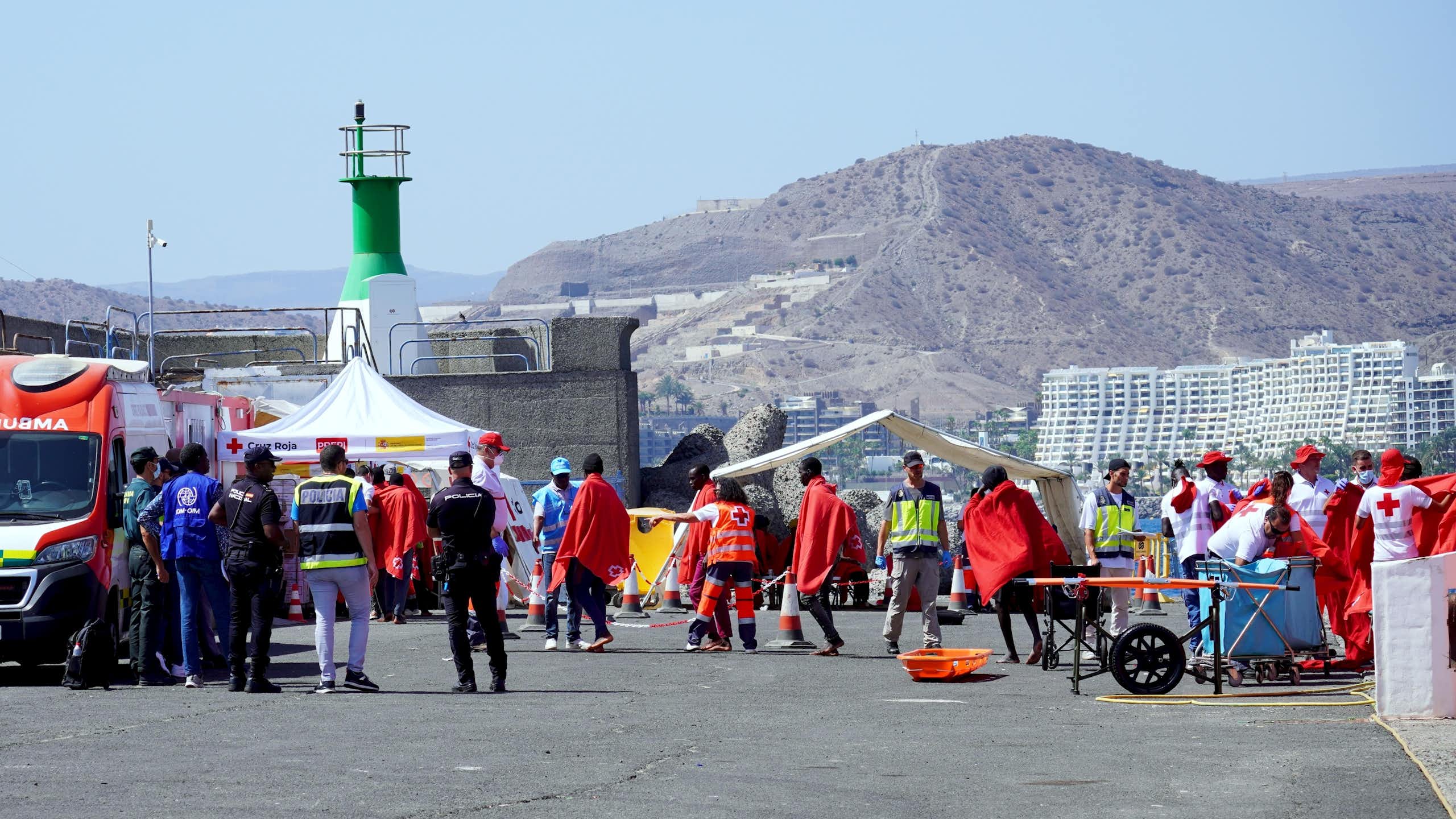 Migrants wrapped ni red blankets and Spanish police Civil Guard officers.