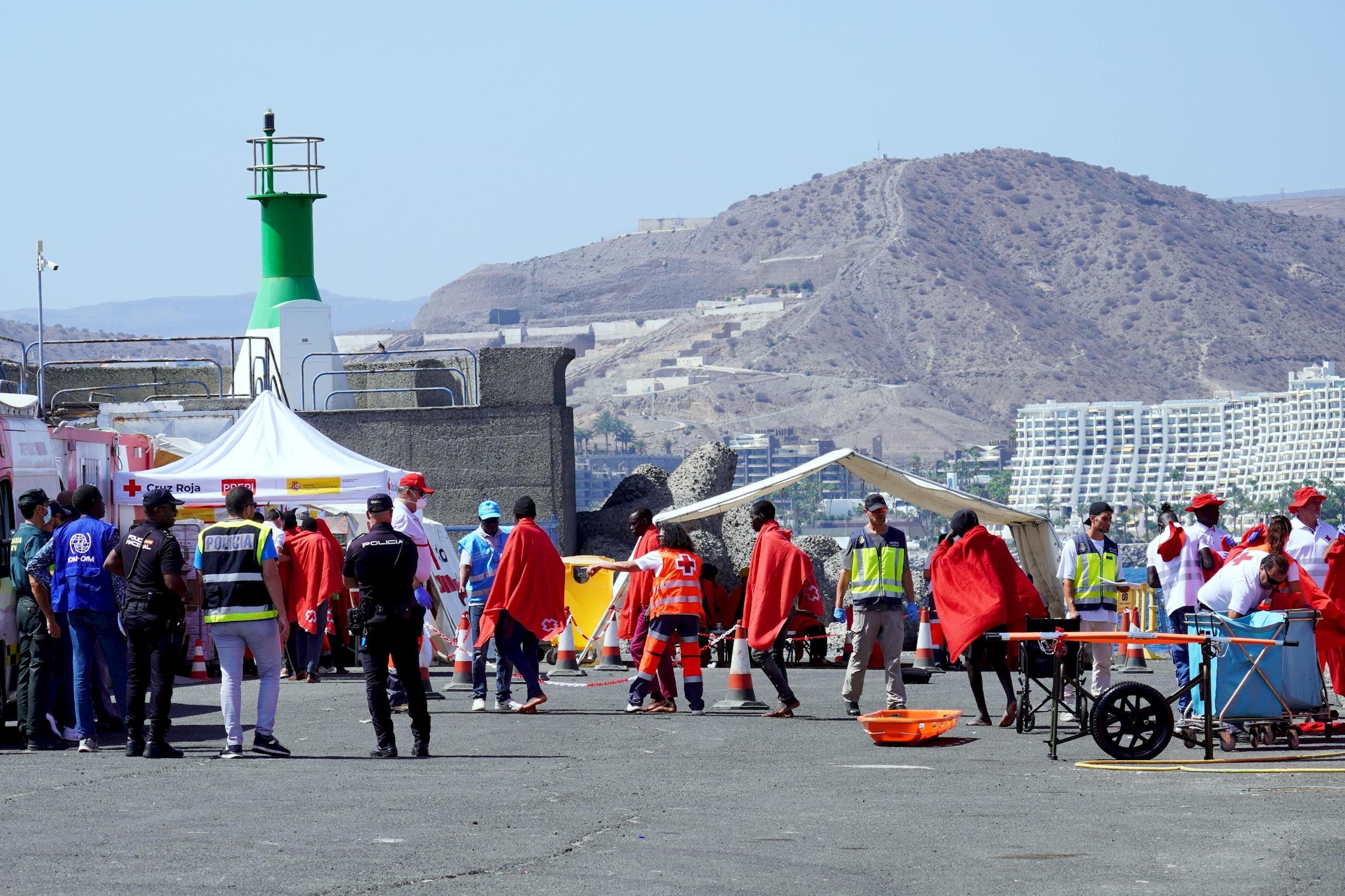 Migrants wrapped ni red blankets and Spanish police Civil Guard officers.