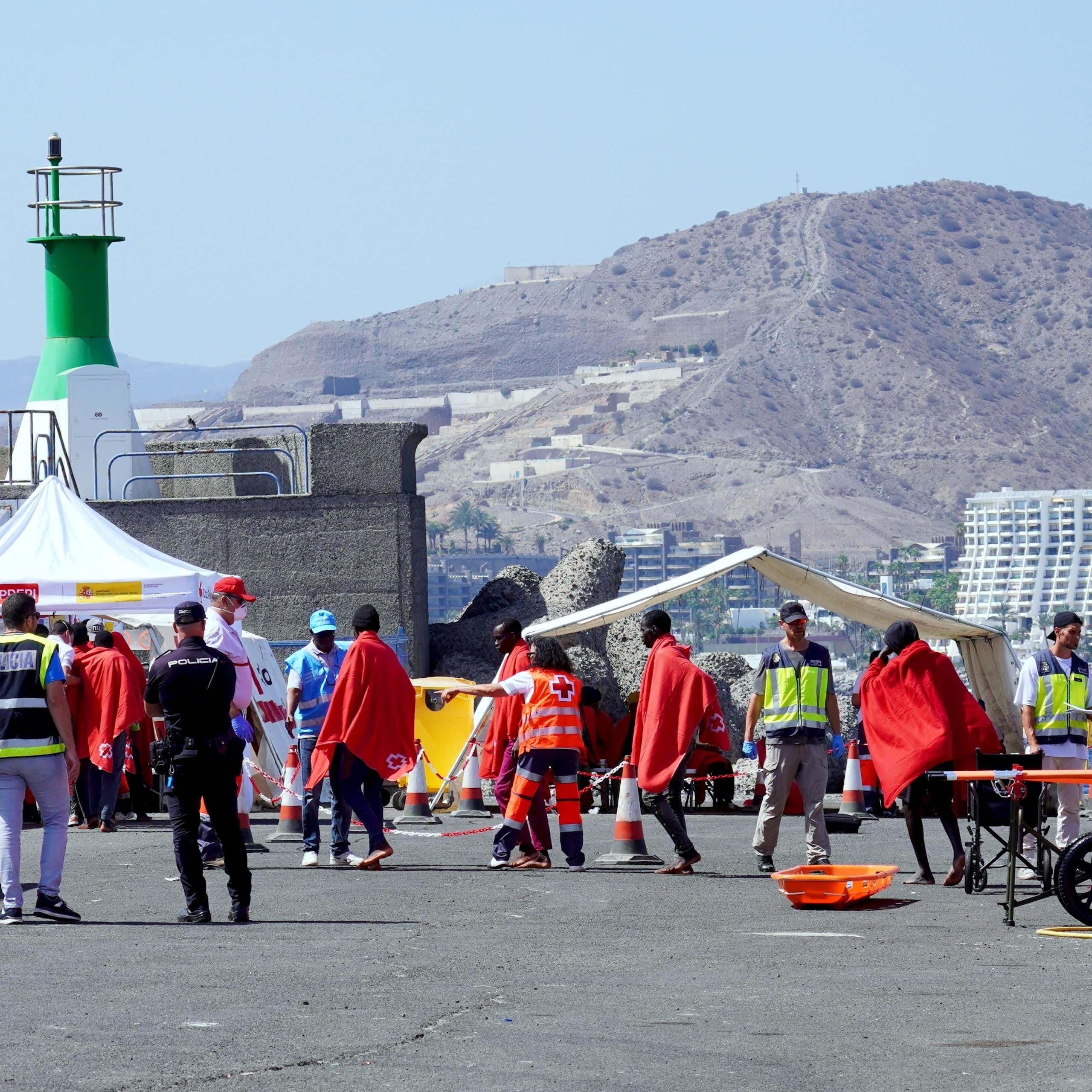 Migrants wrapped ni red blankets and Spanish police Civil Guard officers.