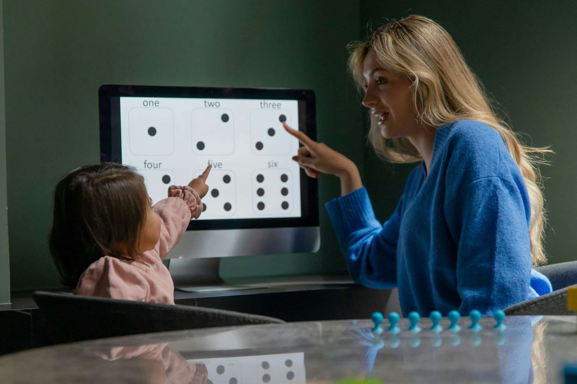 A woman and a child point at a computer screen displaying dice faces and numbers