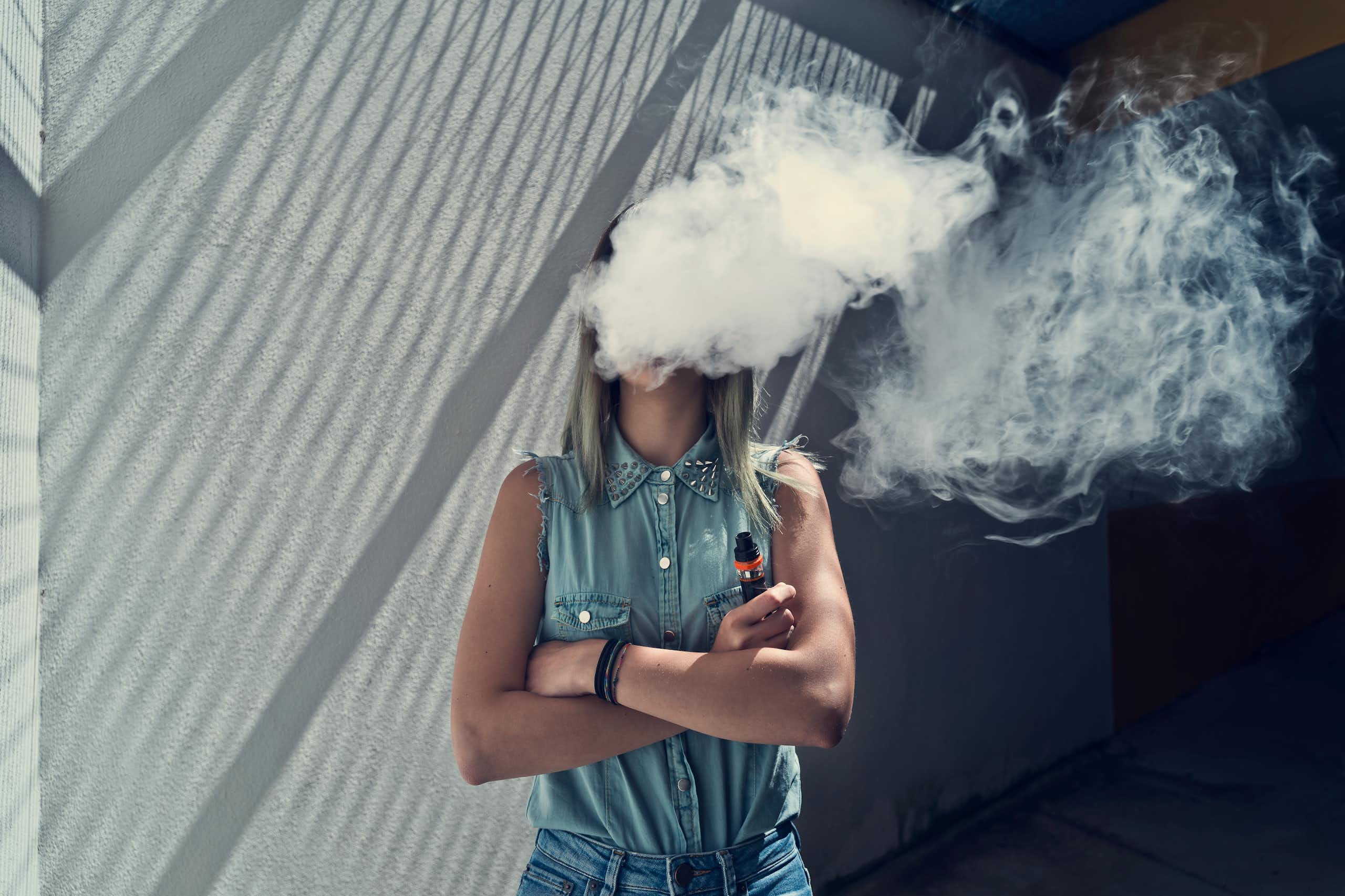 A young person vaping, with a cloud of vapour covering their face