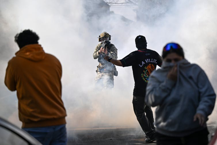 Protesters in a cloud of tear gas face off against a federal agent with a gun.