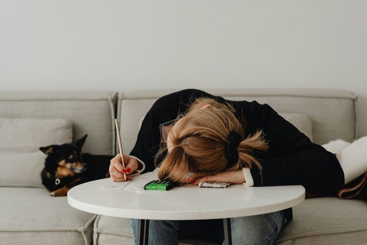 Una mujer sentada con la cabeza gacha sobre una mesa.