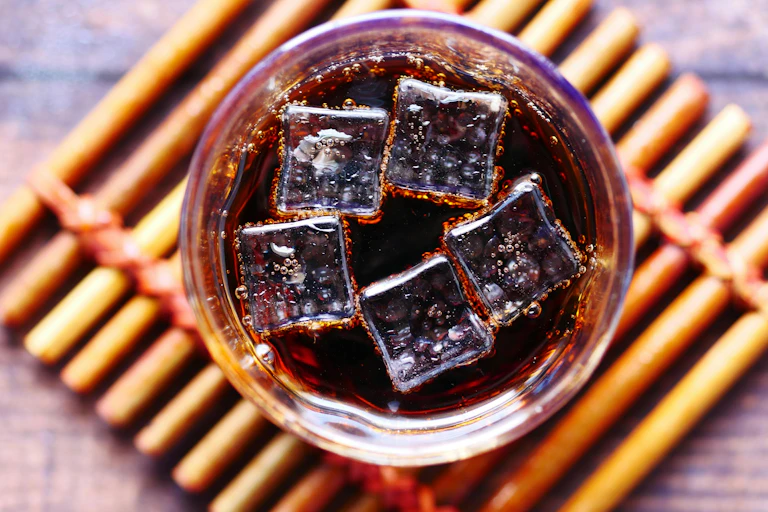 Glass of soft drink, maybe cola, with ice cubes, viewed from above.