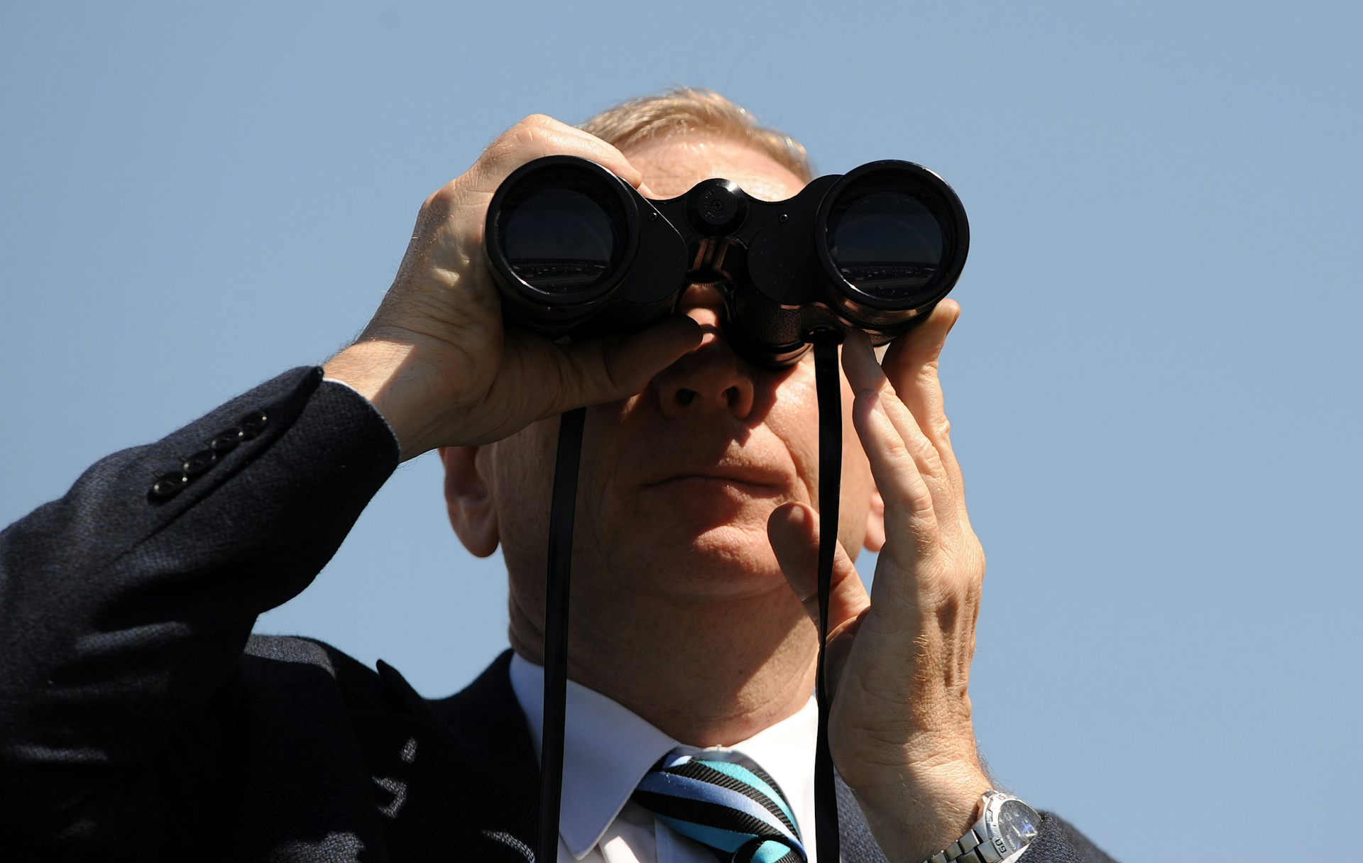 A man at the races, watching through binoculars