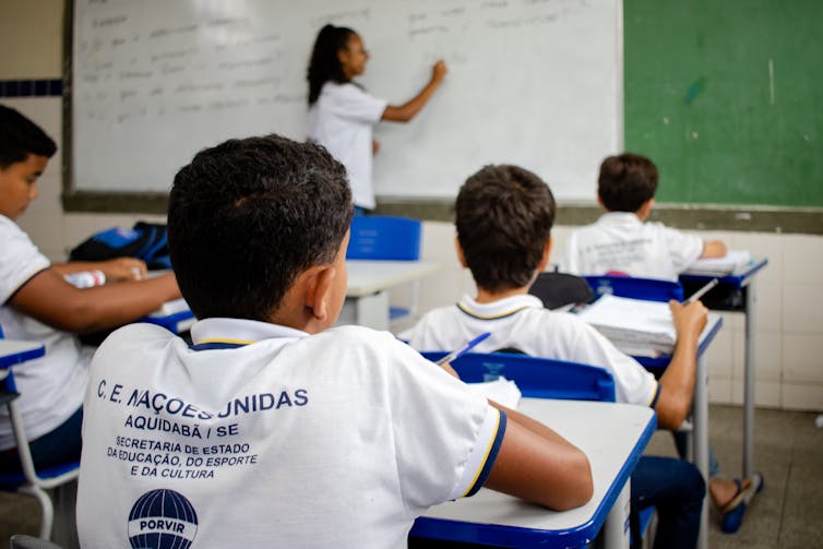 Brazilian school children in white T shirts sat at desks looking at teacher