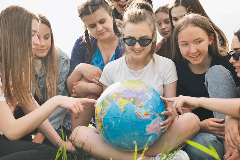 girls sat on lawn looking at and pointing at globe