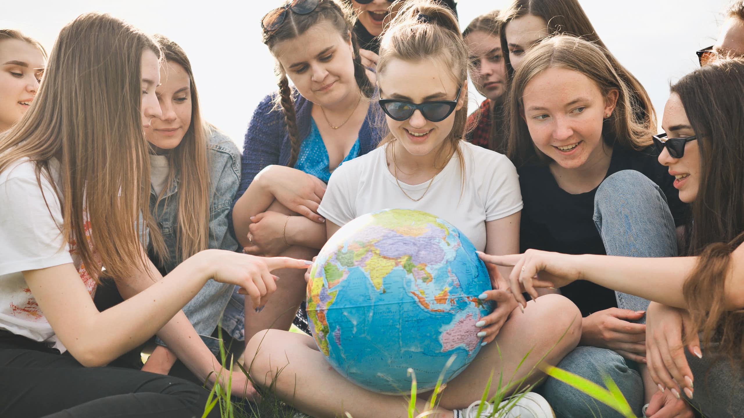 girls sat on lawn looking at and pointing at globe