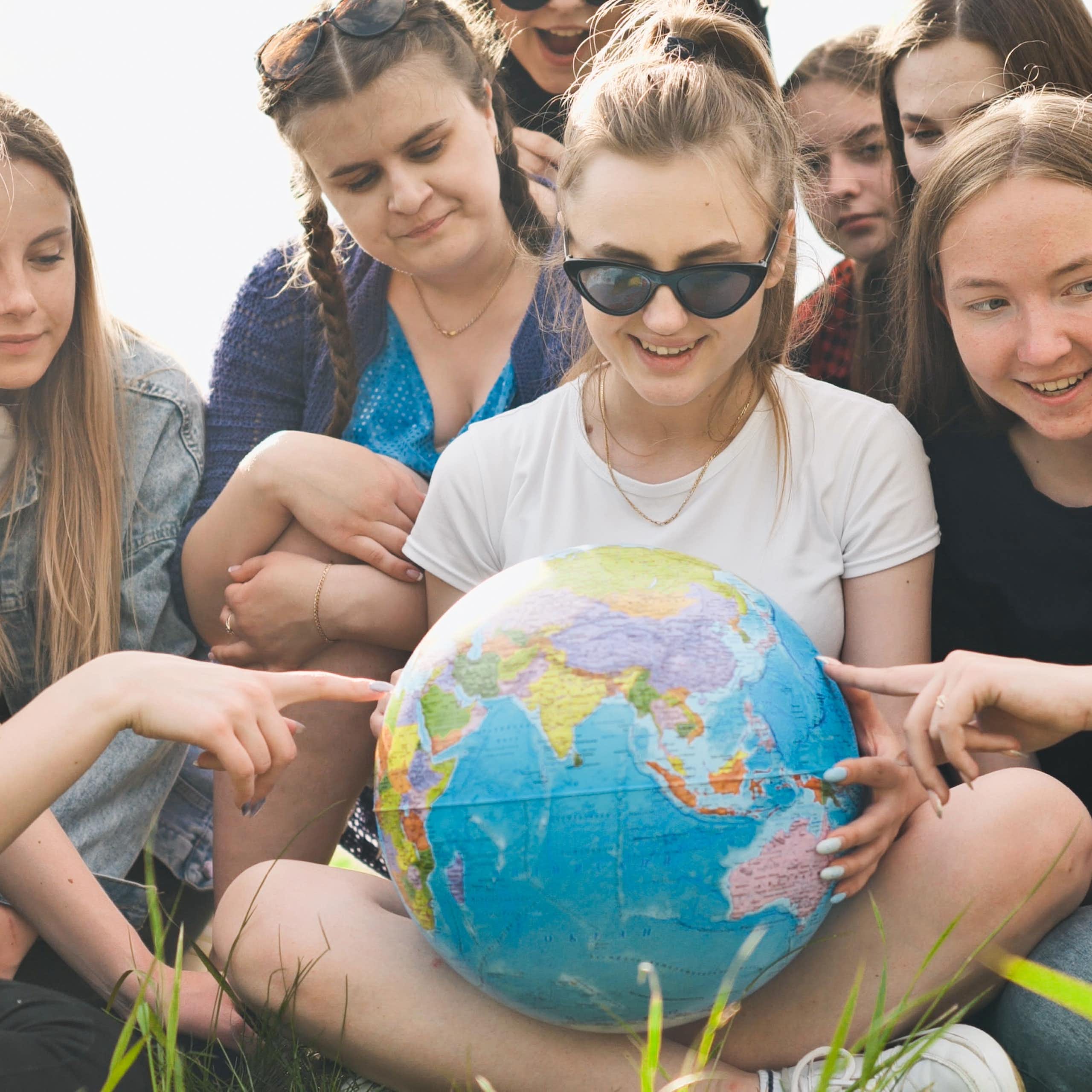 girls sat on lawn looking at and pointing at globe