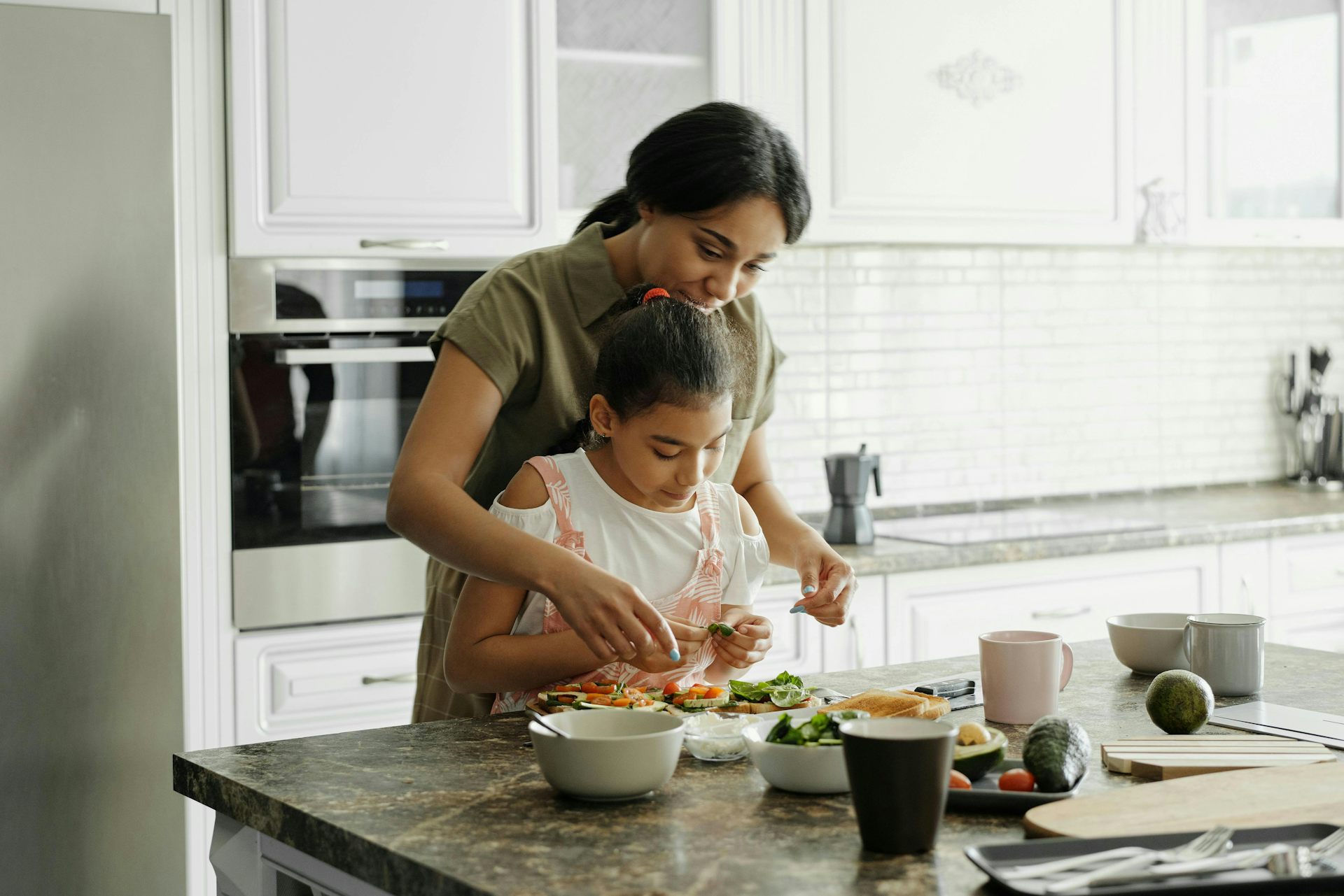Mother and daughter cooking together in white kitchen.