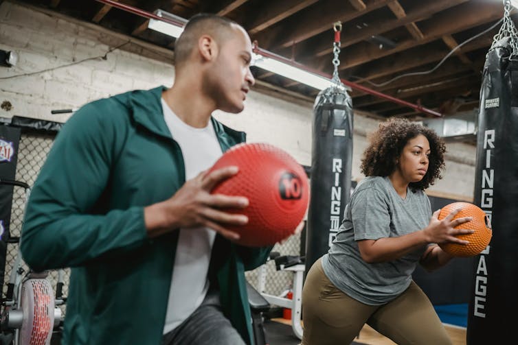 Young man and woman doing exercise with weigh balls in gym.