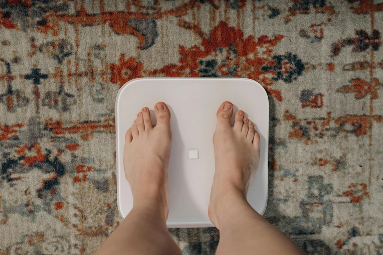 Person's feet on scales on top of patterned rug.