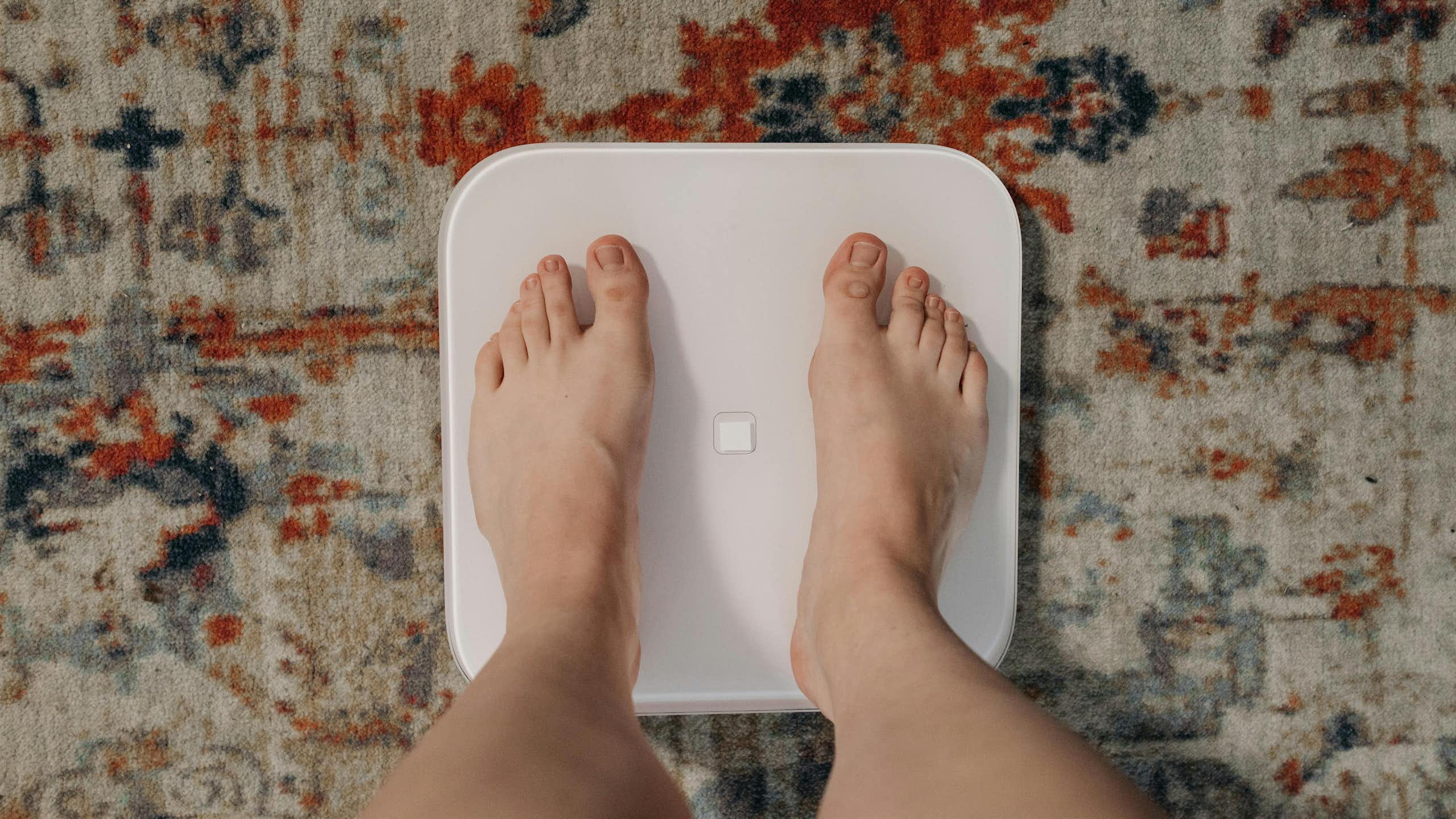 Person's feet on scales on top of patterned rug.