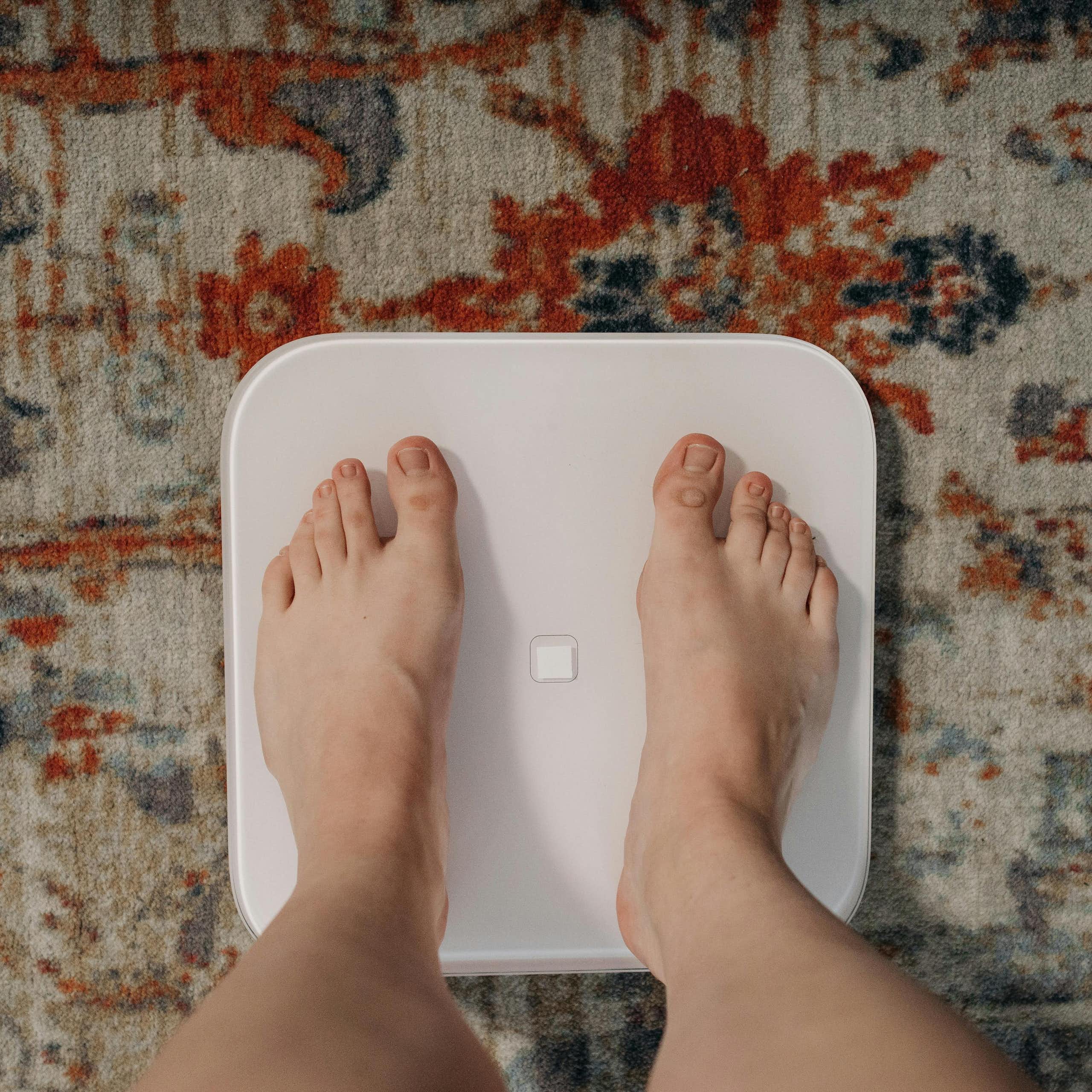 Person's feet on scales on top of patterned rug.