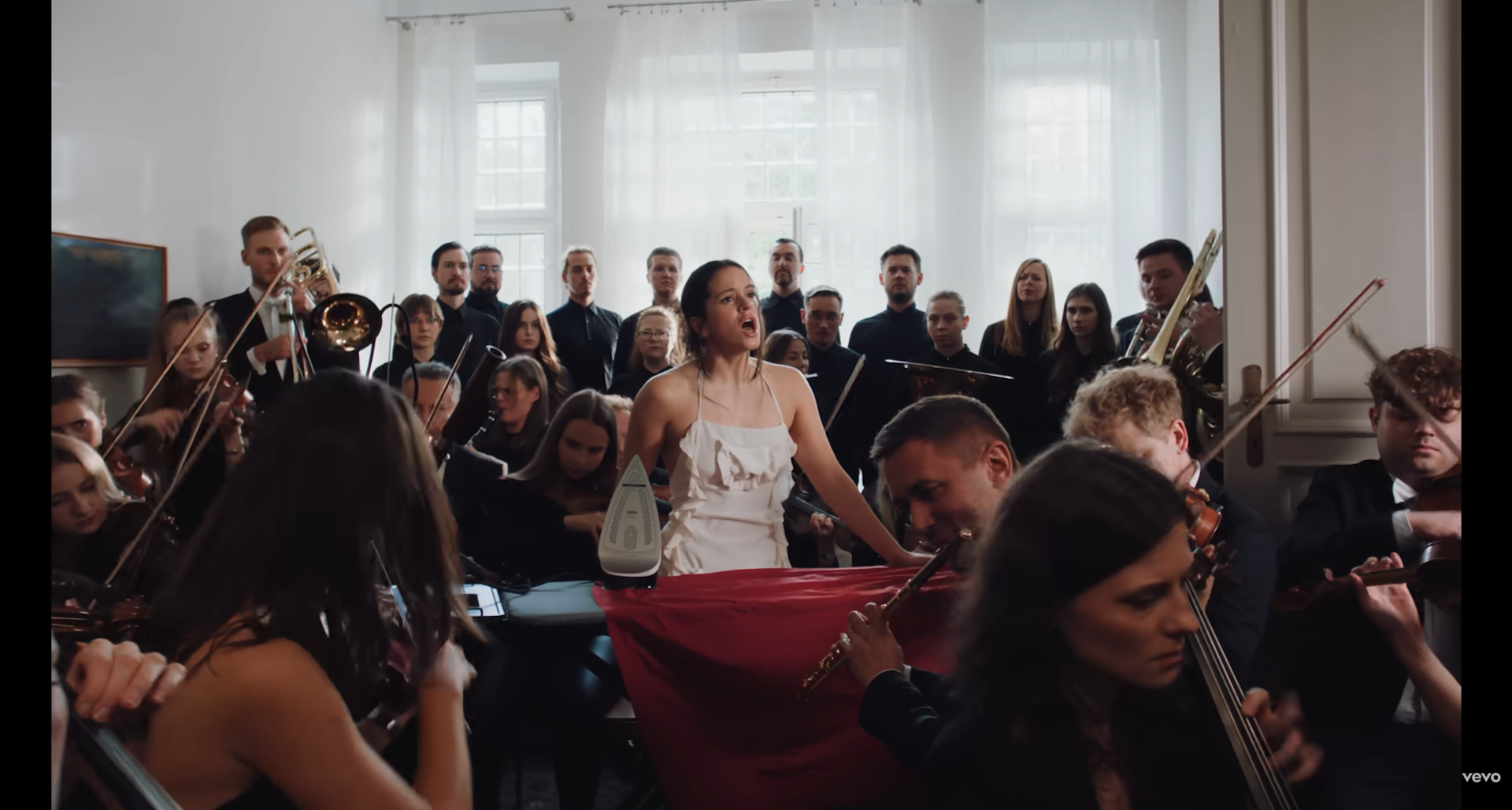 Una mujer canta y plancha la ropa en casa rodeada de una orquesta sinfónica.