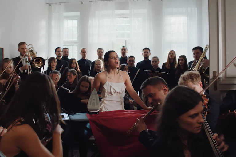 Una mujer canta y plancha la ropa en casa rodeada de una orquesta sinfónica.