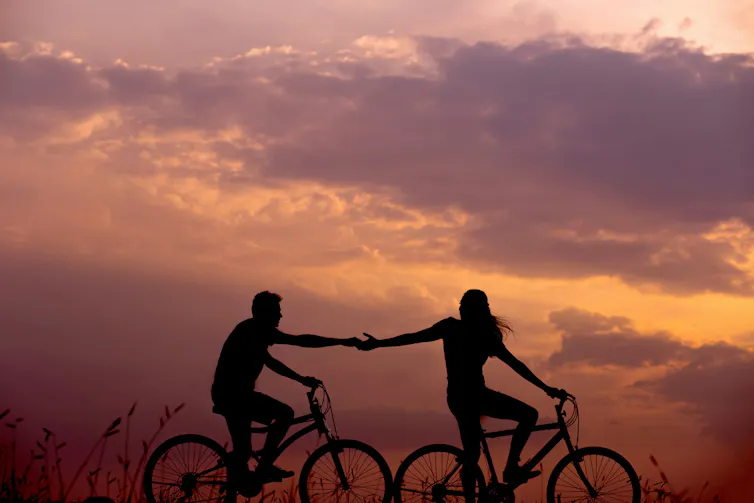 Una pareja se coge de las manos mientras pasea en bici en el atardecer.