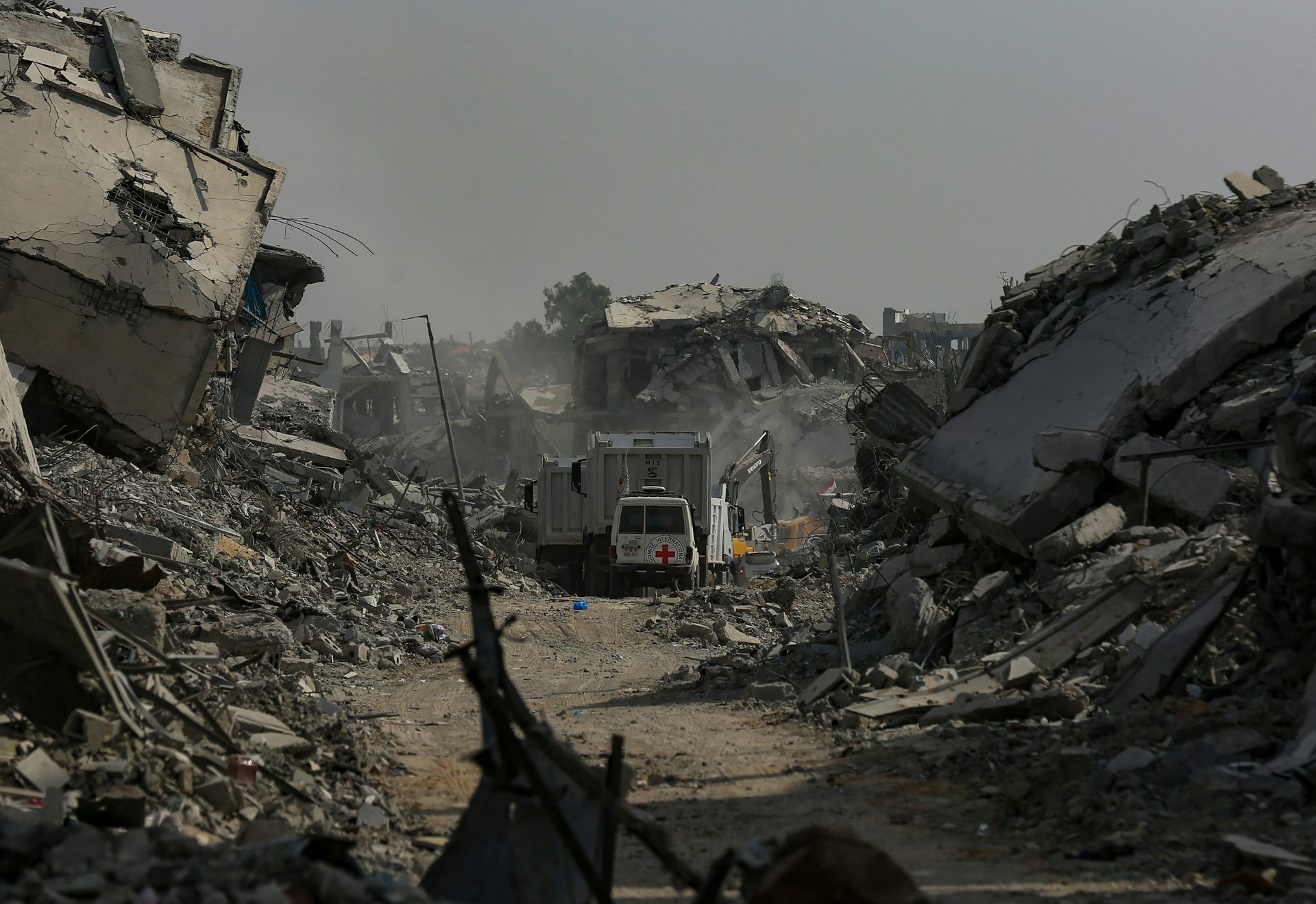 A red cross van drives along a road blocked by rubble.