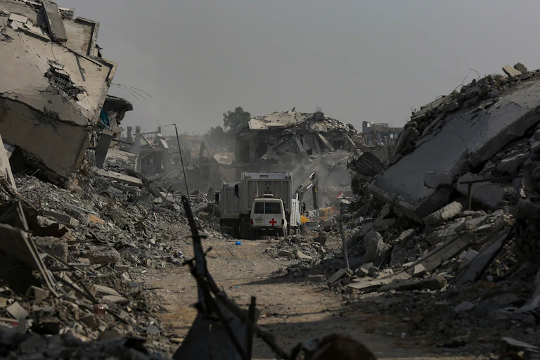 A red cross van drives along a road blocked by rubble.