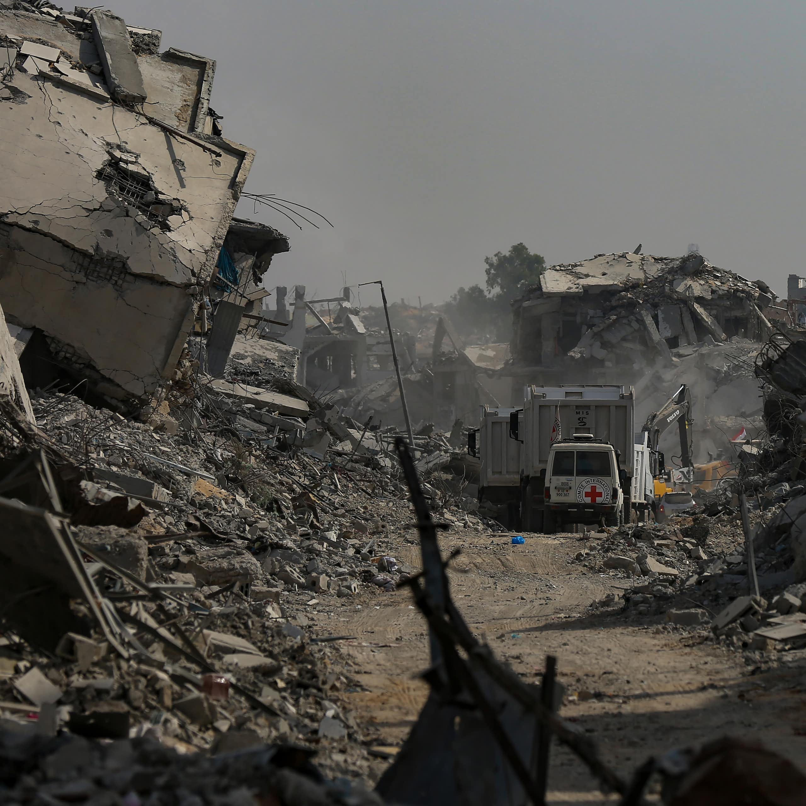 A red cross van drives along a road blocked by rubble.
