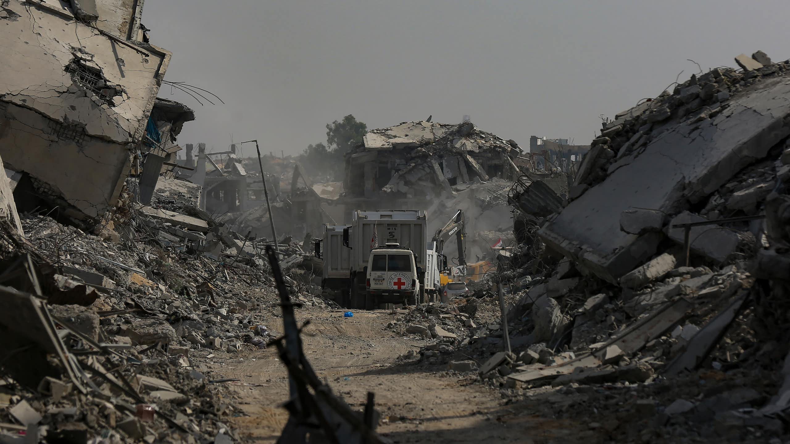 A red cross van drives along a road blocked by rubble.