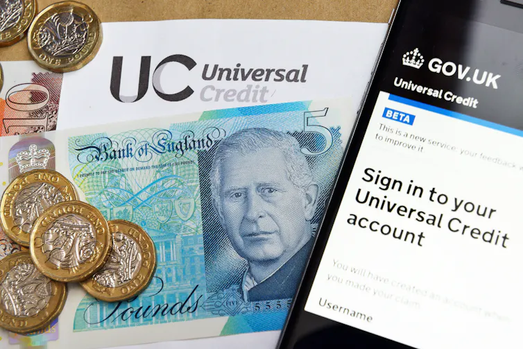phone screen showing universal credit sign-in screen alongside some pound coins and a five-pound note.