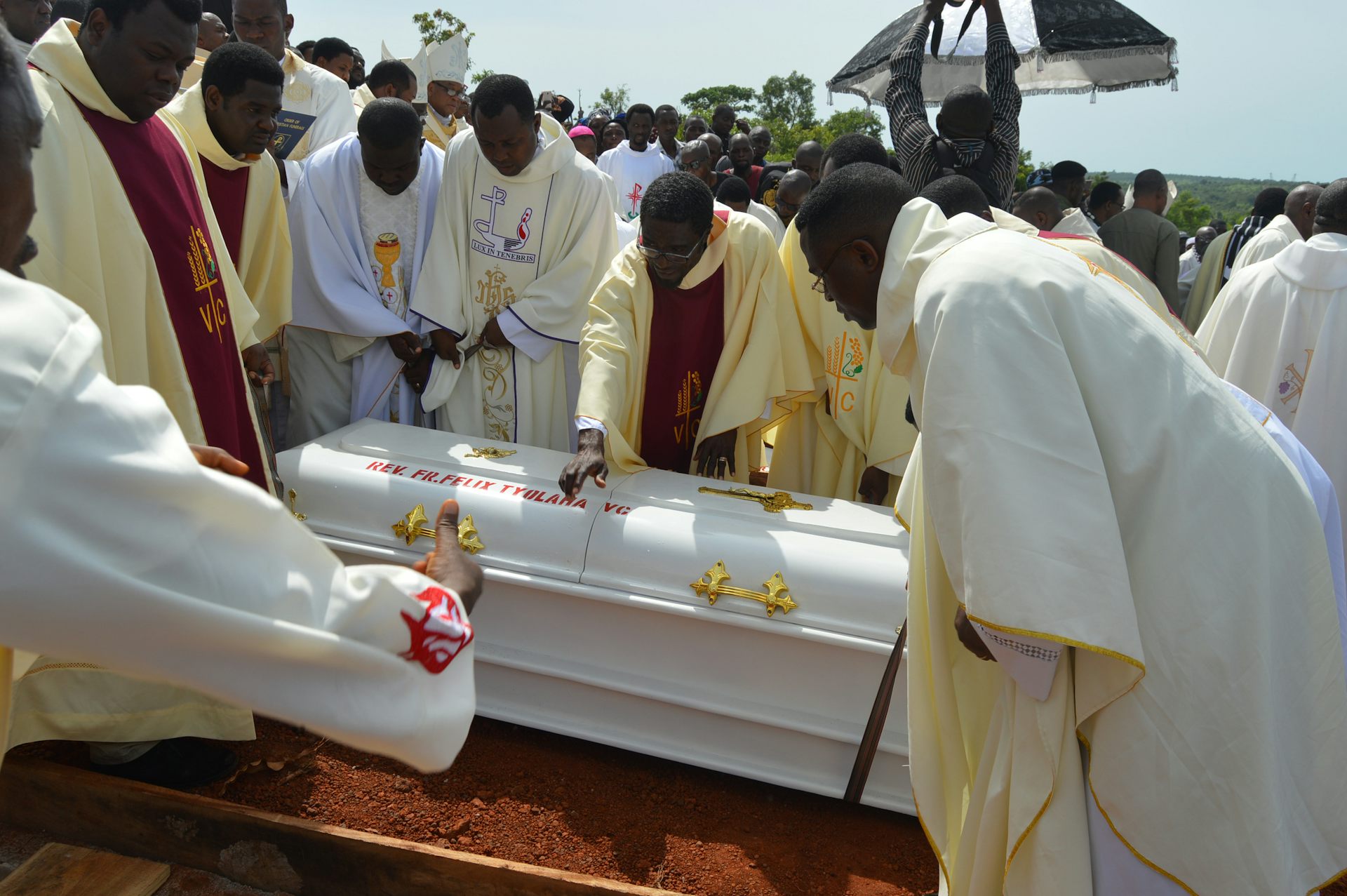 Men in white robes lowering a white coffin into the ground