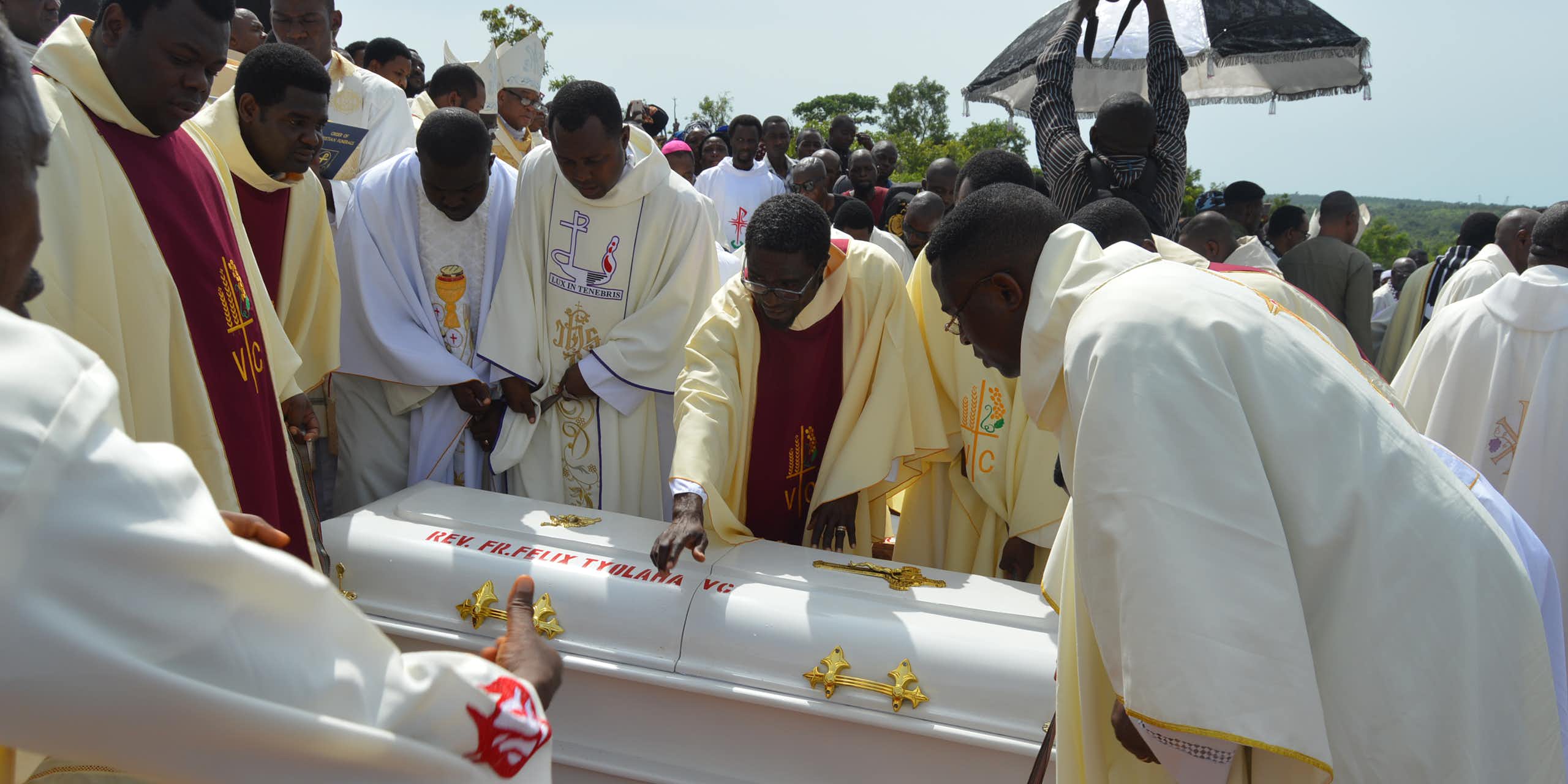 Men in white robes lowering a white coffin into the ground