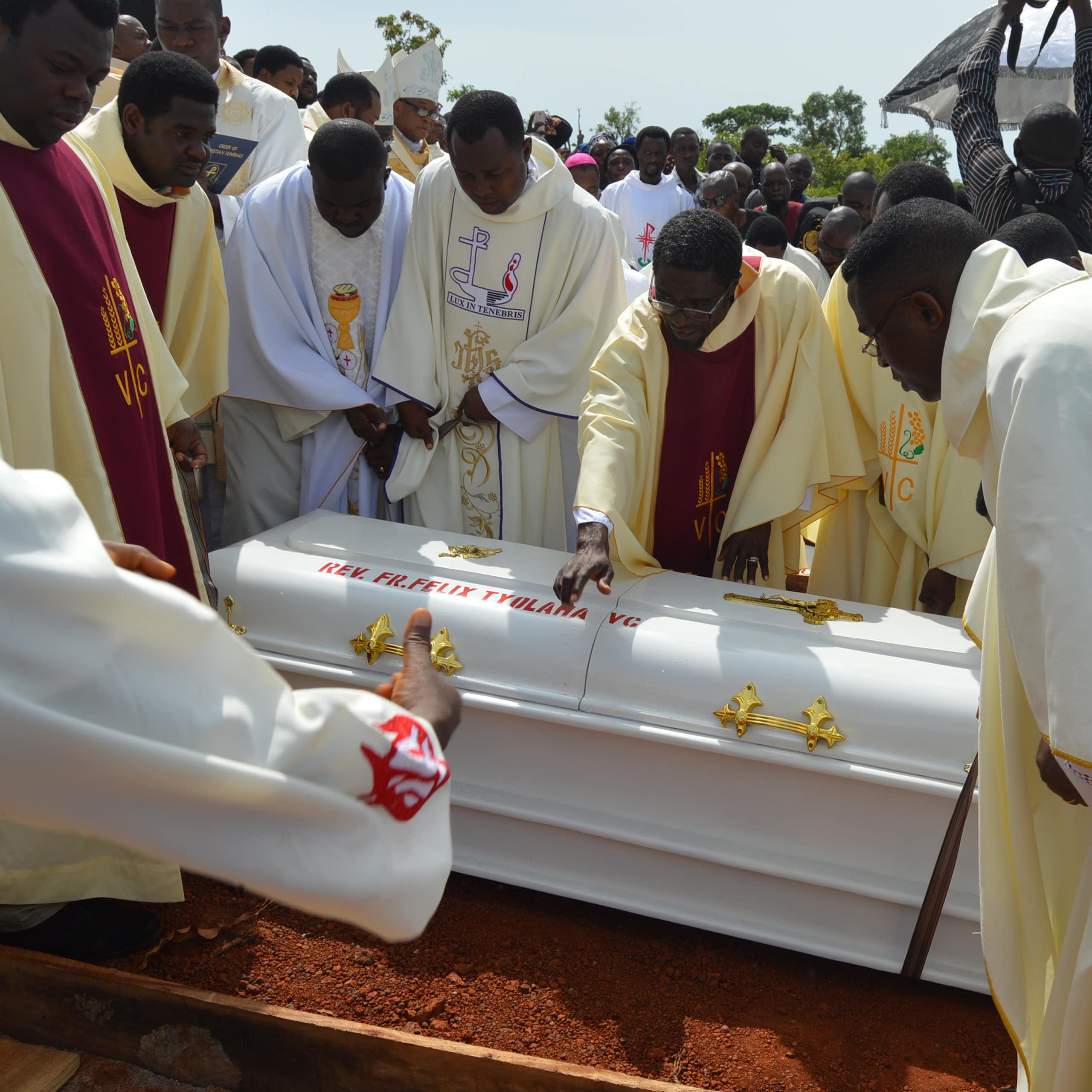 Men in white robes lowering a white coffin into the ground