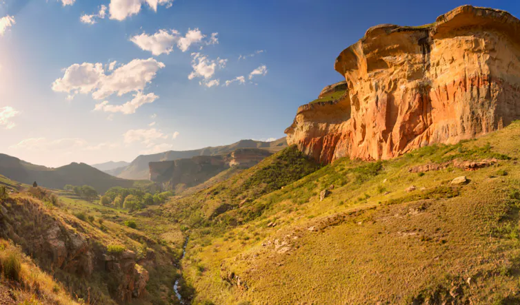 A wild outdoor area of grasslands, a valley and a striking golden rock mountain