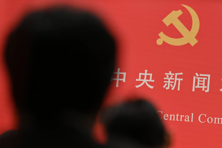 The shadow of a person obscures some Chinese writing and a hammer and sickle emblem.