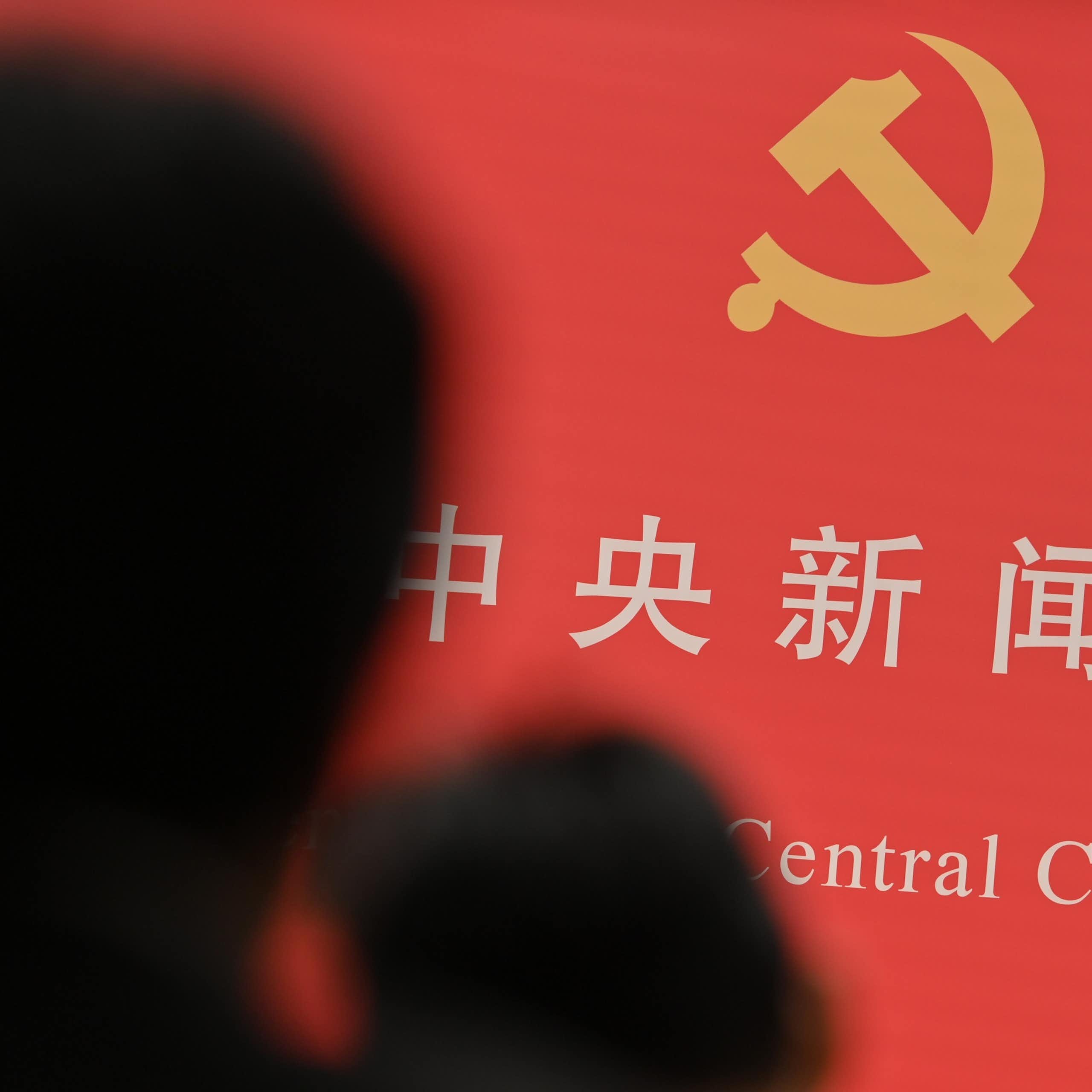 The shadow of a person obscures some Chinese writing and a hammer and sickle emblem.