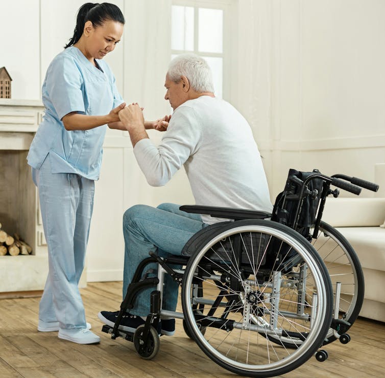 Una mujer ayuda a un hombre en silla de ruedas.