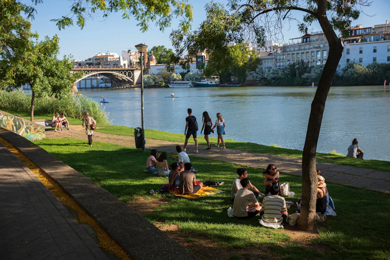 Personas sentadas y paseando a la orilla de un río urbano
