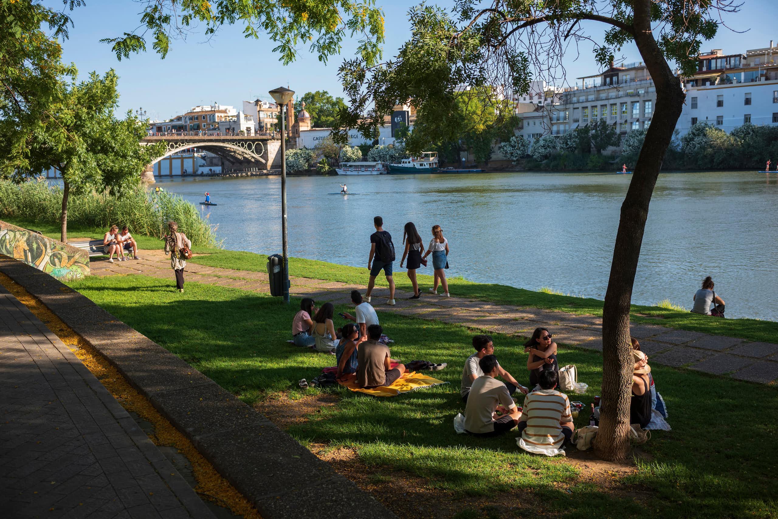 Personas sentadas y paseando a la orilla de un río urbano