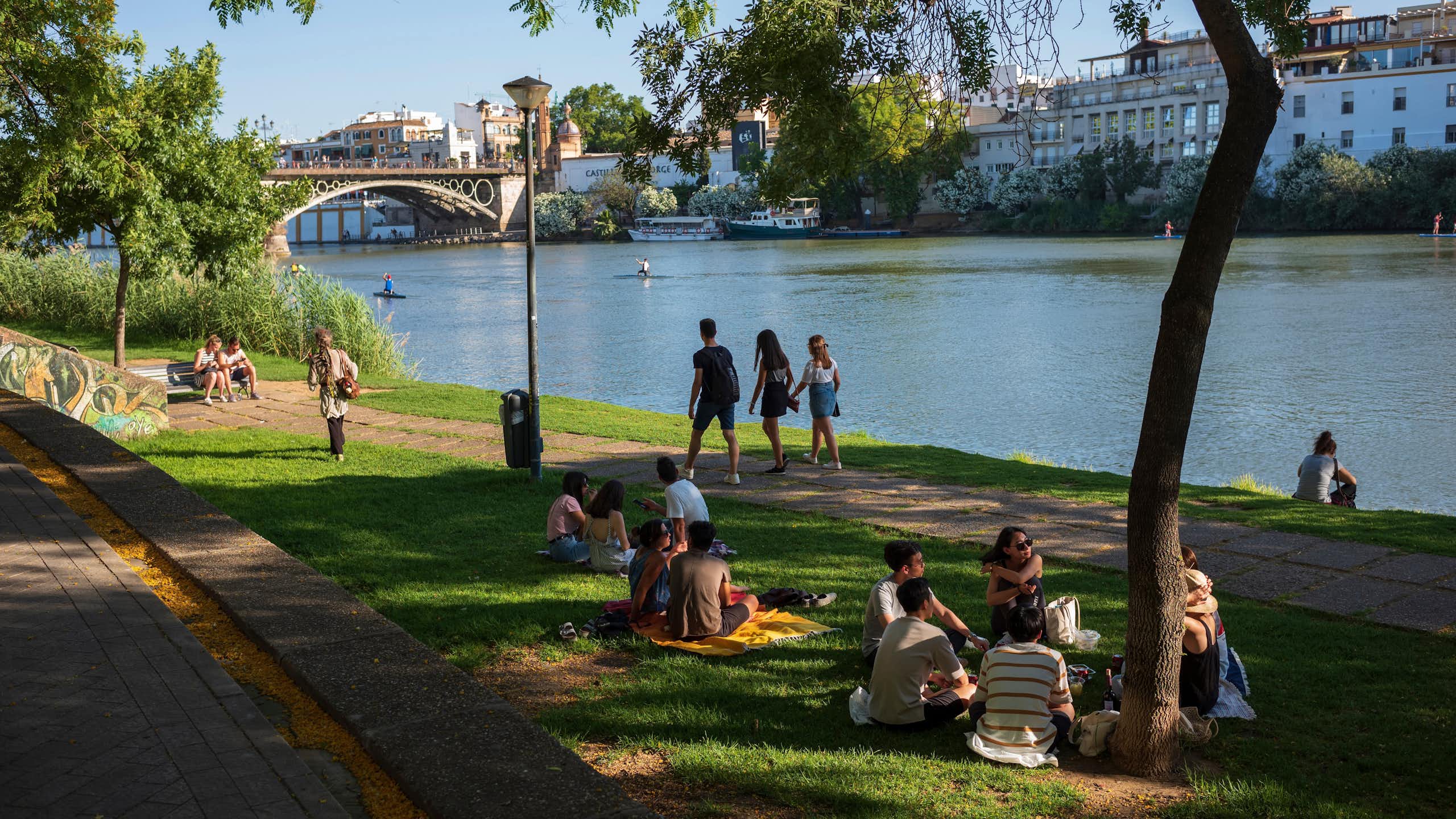 Personas sentadas y paseando a la orilla de un río urbano
