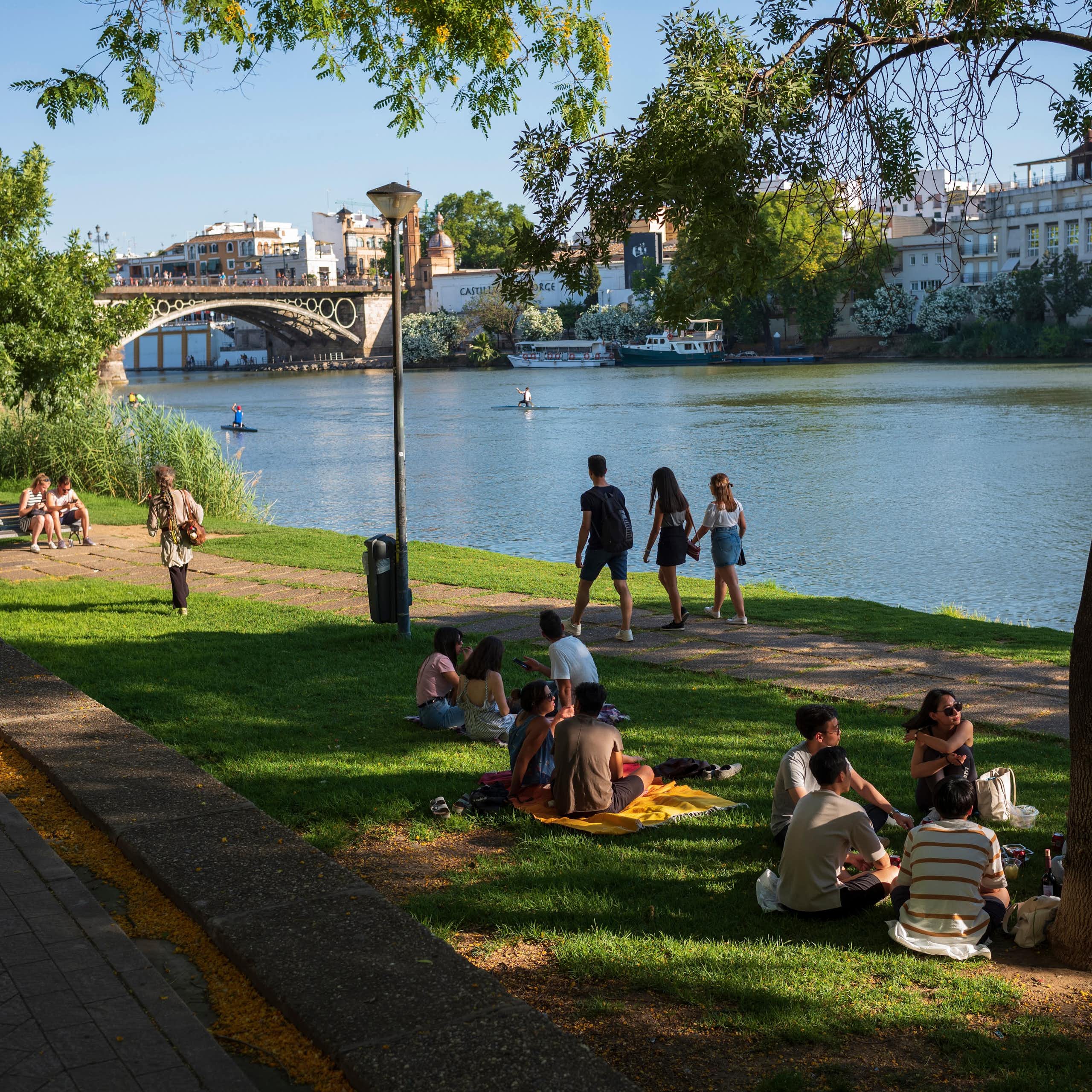 Personas sentadas y paseando a la orilla de un río urbano