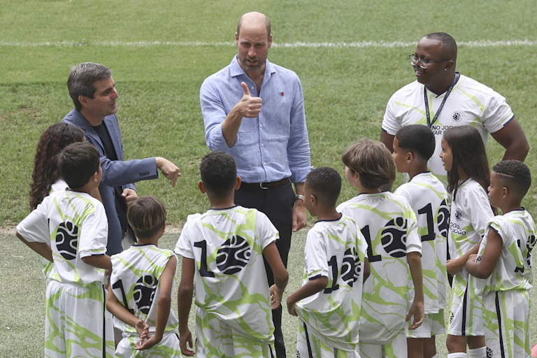 Prince William giving the thumbs up to a group of children in soccer kits.