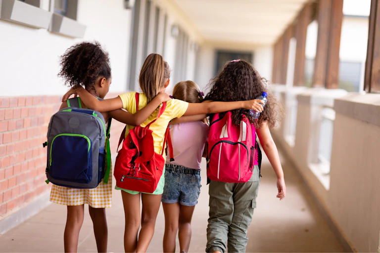 Cuatro niñas caminan abrazadas por el pasillo de una escuela.