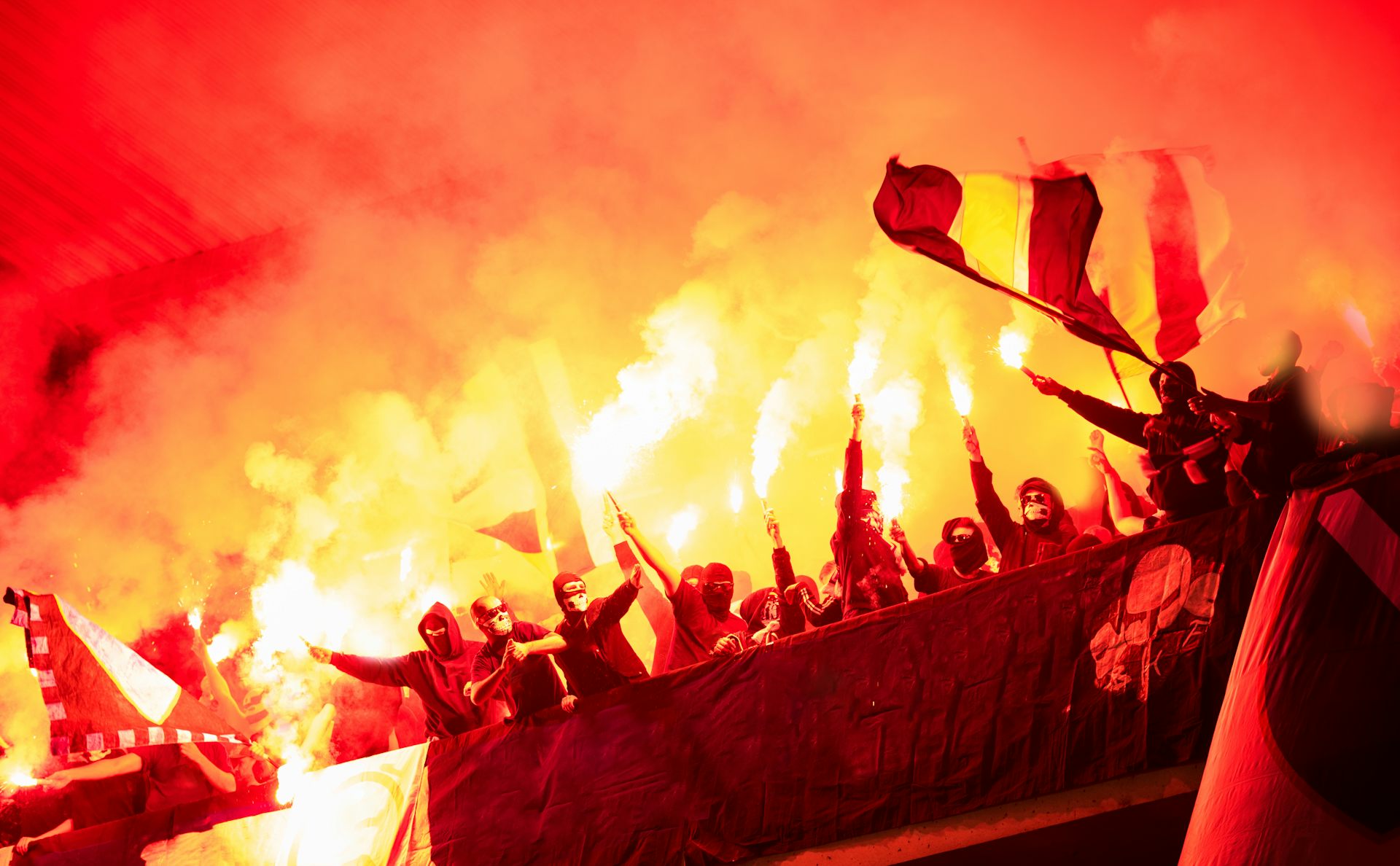 Aficionados con bengalas y banderas en un estadio.