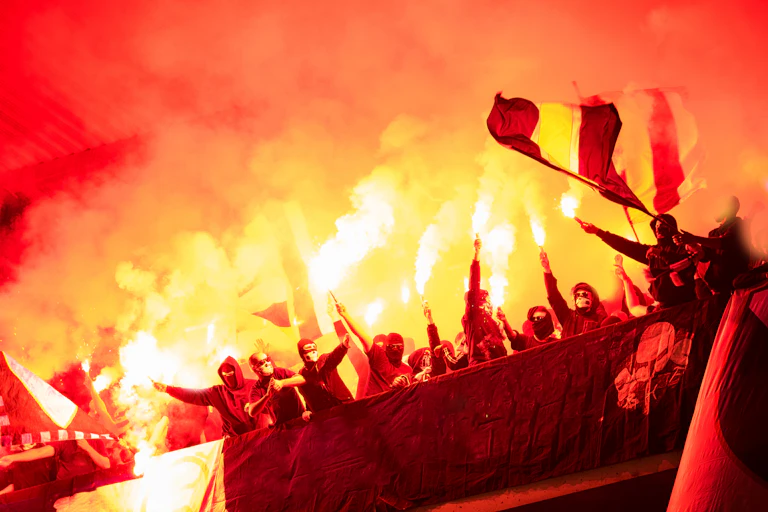 Aficionados con bengalas y banderas en un estadio.