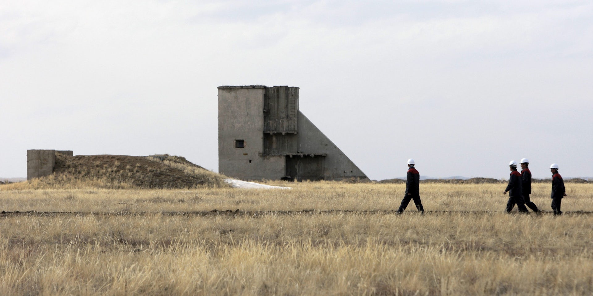 People in hard hats seen near a large concrete tower structure and a barren field.