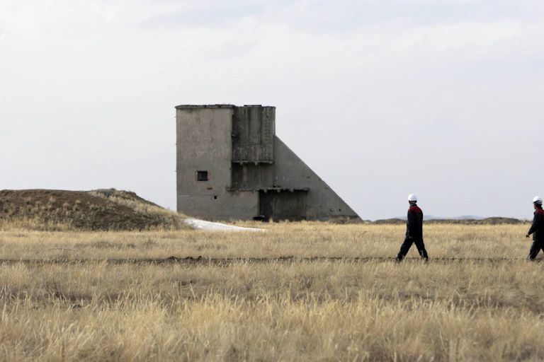 People in hard hats seen near a large concrete tower structure and a barren field.
