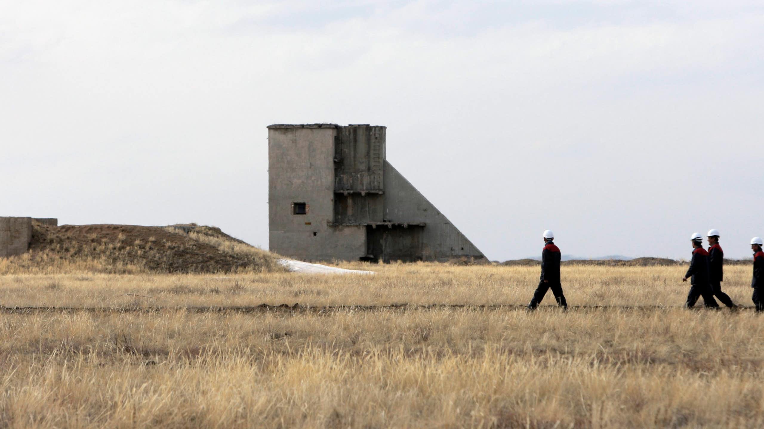 People in hard hats seen near a large concrete tower structure and a barren field.