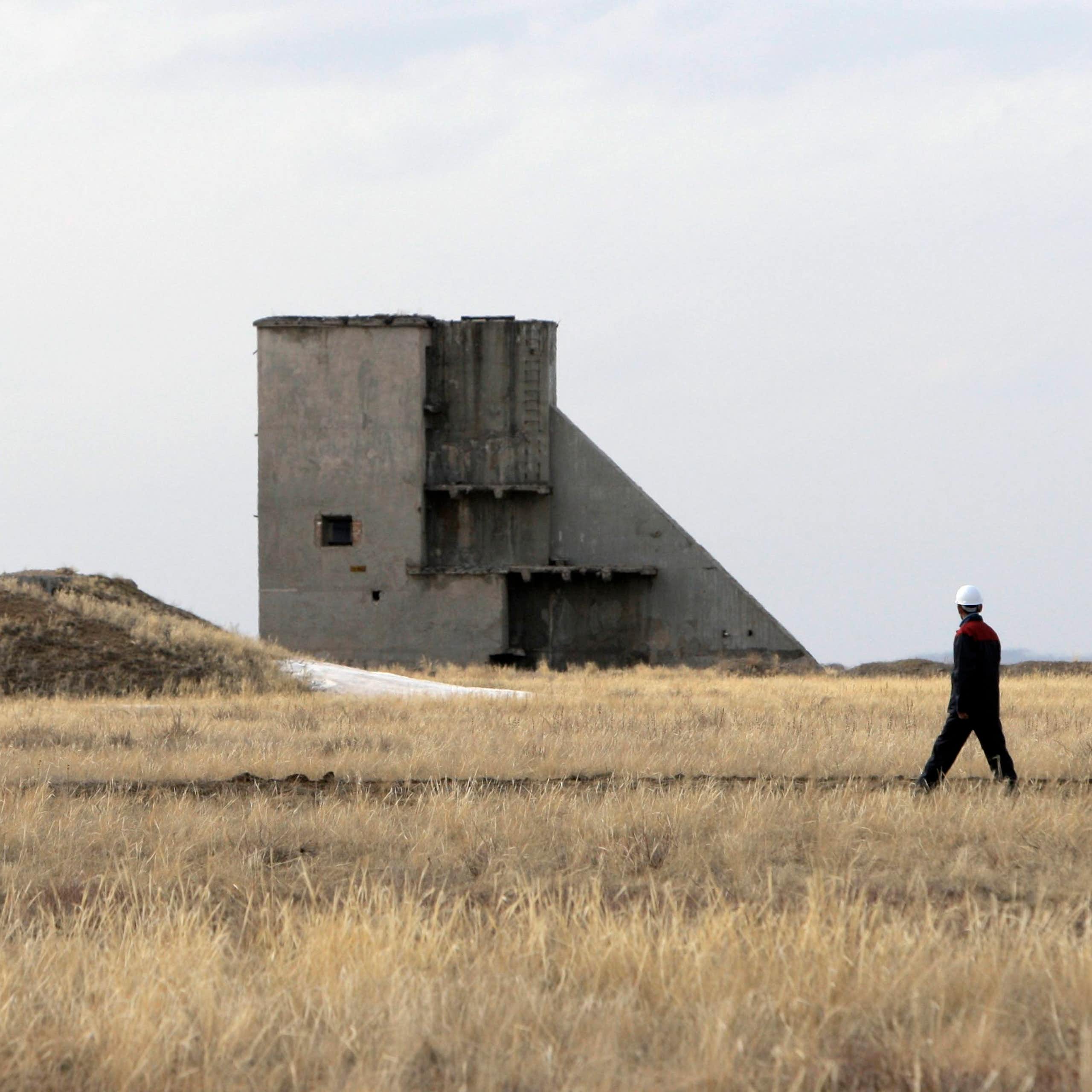 People in hard hats seen near a large concrete tower structure and a barren field.